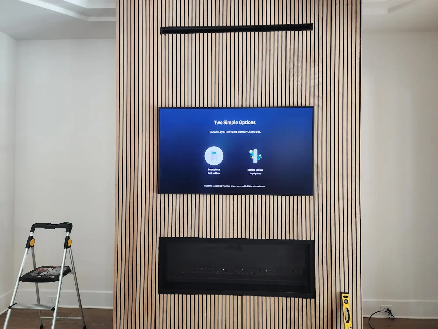 A flat-screen TV mounted flush on a wood slat accent wall above a fireplace, leveled and centered.
